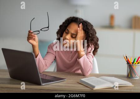 Studente stanco. Studentessa afroamericana che studia online su un computer portatile a casa, esaurita guardando lo schermo Foto Stock