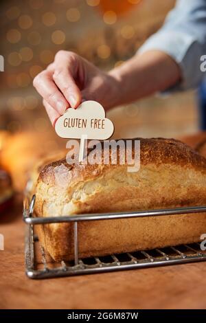 Assistente vendite in panetteria che mette l'etichetta senza glutine in una pagnotta di pasta di farina senza glutine appena sfornata Foto Stock