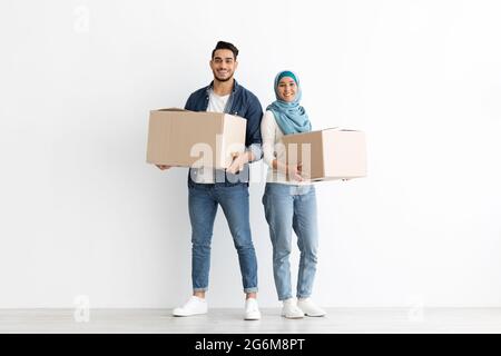 Sorridente coppia musulmana che si sposta in un nuovo appartamento, foto a tutta lunghezza Foto Stock