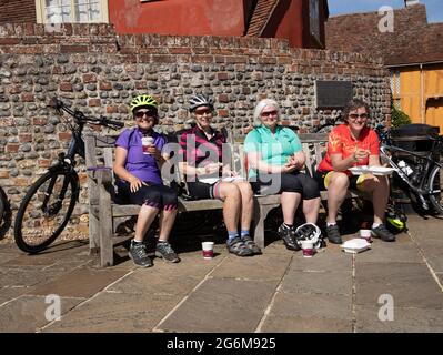 Quattro ciclisti donne anziane felici che mangiano e riposano sulla panchina Lavenham Suffolk Inghilterra Foto Stock
