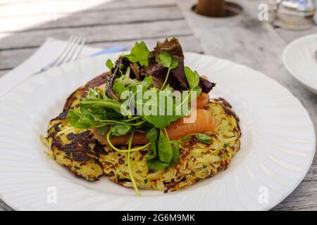 Pranzo leggero di patate arrosti a base di formaggio Racklette, salmone affumicato e foglie di insalata verde serviti all'aperto. Foto Stock