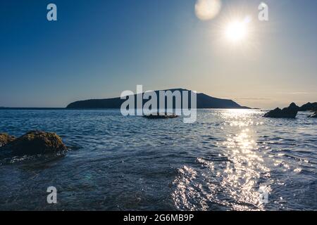 Sole che splende sulla costa selvaggia del Mediterraneo con silhouette di rocce scure, acqua limpida e fascio di sole. Viaggia in Grecia vicino ad Atene. Estate mare natura. Foto Stock