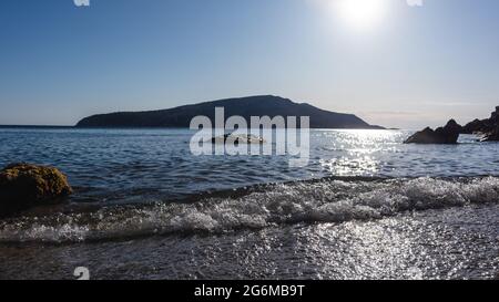 Sole che splende sulla riva selvaggia con onde calme. Mar Mediterraneo con silhouette rocciose, acque limpide e raggi solari. Viaggia in Grecia vicino ad Atene. Estate seasid Foto Stock