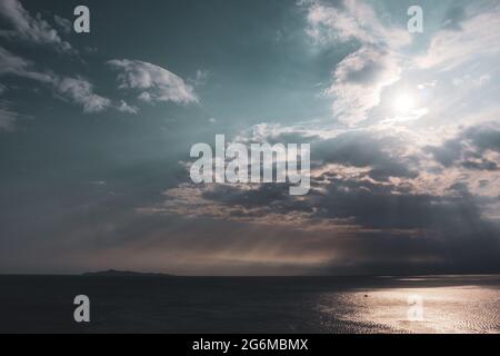 Il sole brilla attraverso le nuvole sul mare in Grecia. Suggestivo paesaggio nuvoloso sulla superficie mediterranea dell'acqua marina. Colore classificato Foto Stock