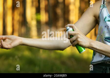 donna che applica lo spray repellente per insetti e zanzare sulla mano nella foresta Foto Stock