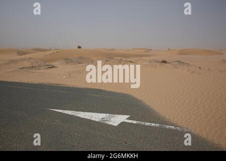 Una freccia bianca sulla strada parzialmente coperta di sabbia a seguito di una tempesta di sabbia a Dubai, Emirati Arabi Uniti. Foto Stock