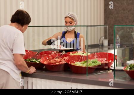 Kemer, Turchia - 24 maggio 2021: La donna mascherata serve verdure per prelevare dal buffet per il sistema alberghiero di tutto compreso. Spazio di copia. Qualità elevata Foto Stock