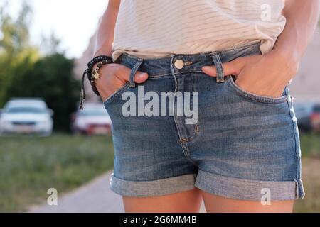 Donna ha bloccato le mani nelle tasche di pantaloncini in denim mentre si è in piedi all'aperto in una giornata estiva. Primo piano. Foto Stock