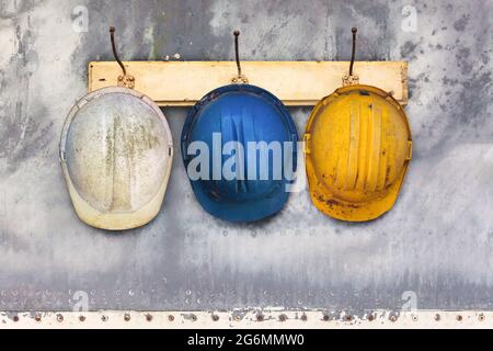 Tre caschi da costruzione appesi su una vecchia rastrelliera in legno Foto Stock