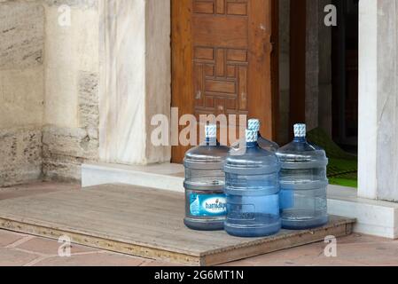 Bottiglioni in policarbonato di plastica lasciati davanti a una porta aperta di un edificio. Consegnato da un'azienda di servizi di acqua potabile. Foto Stock