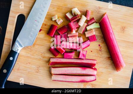 Steli di rabarbaro tritati su un tagliere di bambù: Tritare il rabarbaro con un coltello dello chef di Santoku Foto Stock