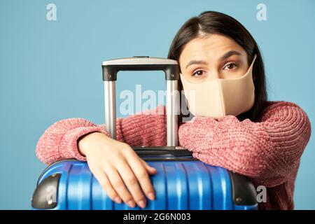 Donna stanca in maschera protettiva vicino ai bagagli Foto Stock