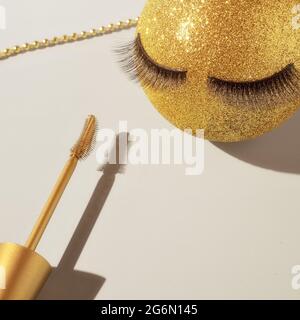 Mascara e una palla di Natale dorata con ciglia false. Il concetto di trucco festivo per le donne. Servizio di make-up per artisti Foto Stock