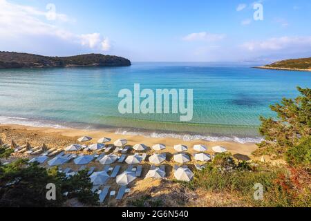 Fantastica sabbia bianca, mare e montagna. Spiaggia vuota con ombrelloni e sdraio chiusi. 2020 viaggio estivo in quarantena. Luoghi relax isola Creta, G. Foto Stock