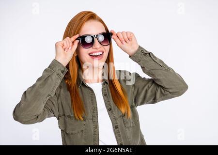 Ritratto di attraente allegra sognante ragazza capelli rossi che tocca le specifiche avendo divertimento isolato su sfondo bianco chiaro colore Foto Stock