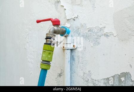 Il rubinetto in ottone con l'adattatore per il collegamento al tubo flessibile da utilizzare in giardino vicino alla parete bianca della casa cittadina, vista frontale con lo spazio per la copia. Foto Stock