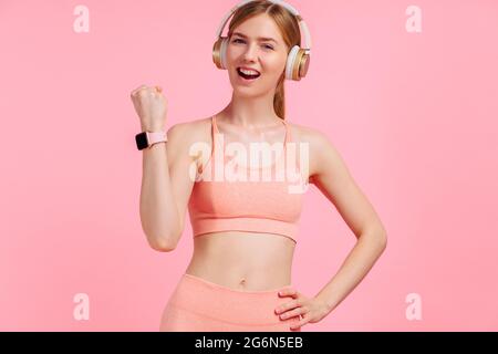 Felice donna sportiva in tuta che celebra il suo successo su isolato sfondo rosa Foto Stock