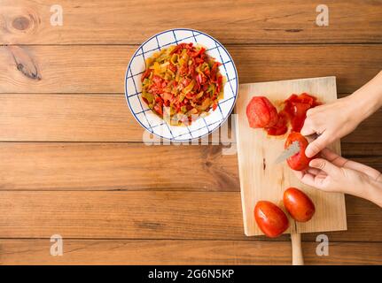 Dettaglio delle mani di una donna che spellano i pomodori con un coltello. Preparazione di peperoni arrostiti, un piatto tipico della cucina spagnola e andalusa. Foto Stock