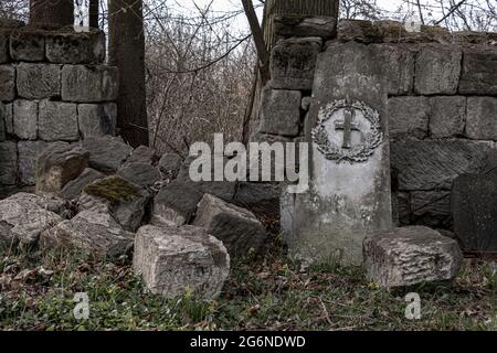 Un muro di pietra demolito con una lapide danneggiata in un cimitero Foto Stock