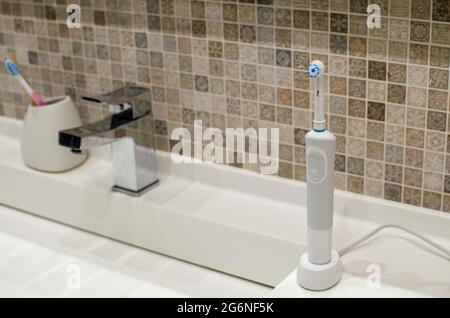 Spazzolino elettrico ricaricabile, primo piano. Sullo sfondo di un bagno in bianco. Rubinetto d'acqua e lavello bianco. Foto Stock