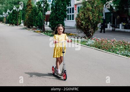 una ragazza guida uno scooter, una passeggiata in famiglia in una giornata estiva sugli scooter, uno stile di vita sano e di ricreazione Foto Stock