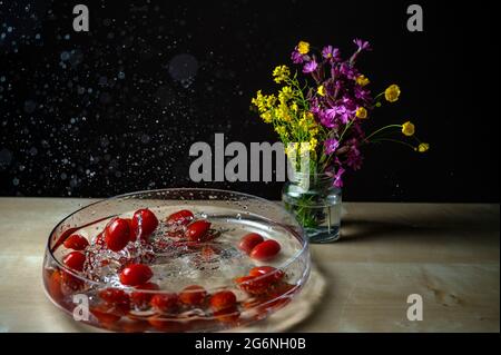 Primo piano di un gruppo di tomatos di prugne (pomodoro bambino, pomodoro ciliegia) rosso fresco che cade sul recipiente dell'acqua con acqua splash copyspace fiore backgro Foto Stock