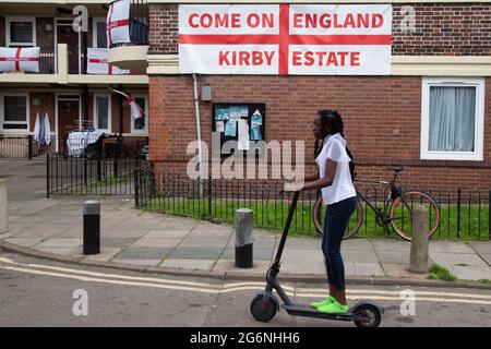 Londra, Regno Unito. 07 luglio 2021. Una ragazza cavalcava uno scooter davanti alle bandiere inglesi e si accamparono drappeggiato sui balconi e attaccati alle pareti della tenuta Kirby a Bermondsey, a sud-est di Londra. Un'abitazione è stata coperta con bandiere inglesi prima della partita semifinale contro la Danimarca. (Foto di Thabo Jaiyesimi/SOPA Images/Sipa USA) Credit: Sipa USA/Alamy Live News Foto Stock