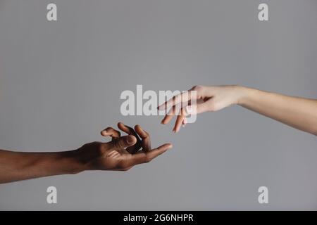 Mani maschili e femminili che si allungano l'una verso l'altra isolate su sfondo grigio. Foto Stock