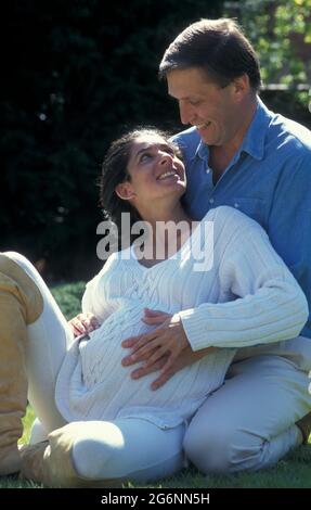 donna incinta anglo-asiatica molto incinta seduta fuori con il suo compagno Foto Stock