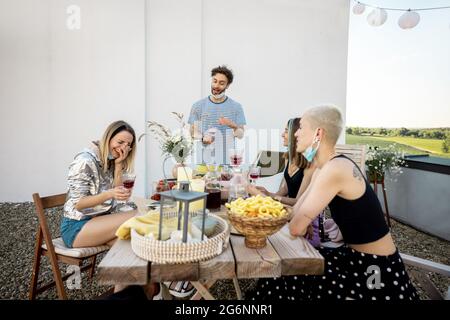Gli amici in maschere di faccia hanno una cena festosa all'aperto Foto Stock