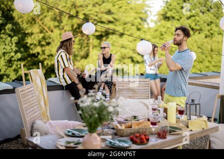 Giovani amici alla moda che hanno una cena festosa sulla terrazza sul tetto Foto Stock