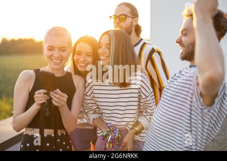 I giovani amici si divertono sulla terrazza sul tetto al tramonto Foto Stock