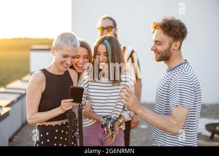 I giovani amici si divertono sulla terrazza sul tetto al tramonto Foto Stock