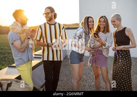 I giovani amici si divertono sulla terrazza sul tetto al tramonto Foto Stock