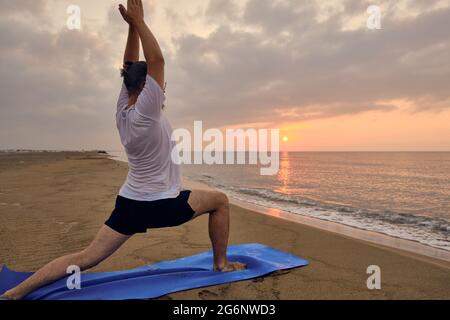 L'uomo pratica guerriero una posa in mare spiaggia Foto Stock