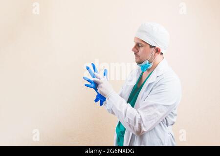 Giovane medico in tuta bianca e maschera protettiva per la respirazione mette i guanti sulle mani su sfondo giallo isolato. Foto Stock