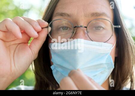 Donna che indossa occhiali da nebbia a causa di indossare una maschera medica. Inconveniente dovuto alla condensa sulle lenti. Primo piano. Foto Stock