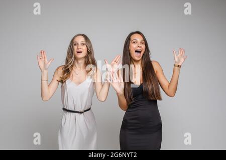 Due belle donne in piedi in studio puntando le dita verso l'alto, isolato su sfondo grigio. Concetto di festa. Spazio di copia Foto Stock