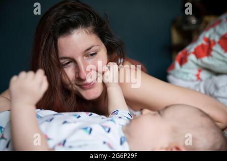 Una madre sdraiata su un letto con il suo bambino Foto Stock