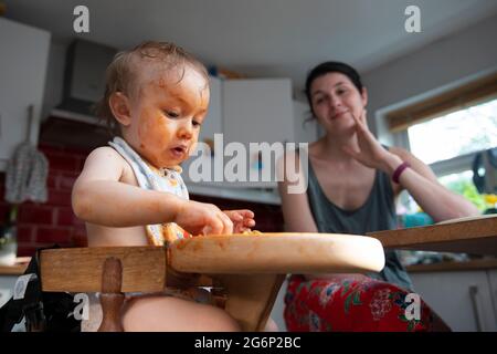 Una madre che guarda il suo bambino mangia in modo disordinato Foto Stock