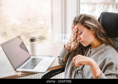 Donna d'affari stanca che lavora da casa al computer portatile e al caffè, guardando preoccupato e stressato. Burnout e ansia, benessere mentale e concetto di salute Foto Stock