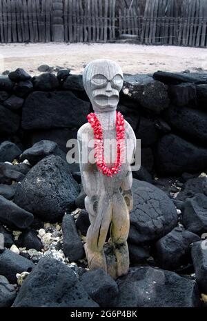 L'antico Tiki si erge sulla guardia del Parco storico Nazionale di Puuhonua o Honaunau sulla Grande Isola delle Hawaii. Una plumeria lei rosa e fresca pende intorno alla sua n Foto Stock