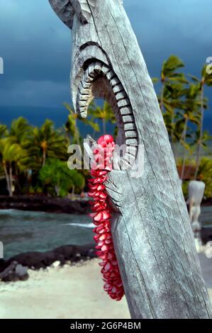 Bella plumeria lei rosa pende dalla bocca aperta di un tiki Hawaiiano a Puuhonua o Honaunau National Historical Park sulla Big Island delle Hawaii. Foto Stock