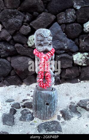 L'antica tigi si erge guardia sulla spiaggia del Parco Nazionale storico di Puuhonua o Honaunau sulla Grande Isola delle Hawaii. Un lei di plumeria rosa è stato l Foto Stock