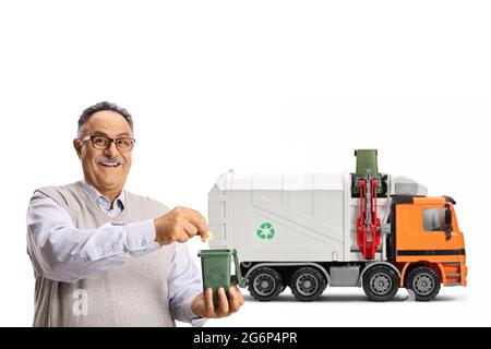 Uomo maturo gettando carta in un piccolo bidone di fronte a un camion spazzatura isolato su sfondo bianco Foto Stock