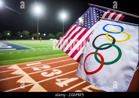 MIAMI, USA - 15 AGOSTO 2019: Un'onda di bandiera olimpica e americana insieme sotto i riflettori di una pista atletica rossa. Foto Stock
