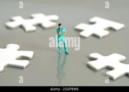Foto di personaggi giocattolo in miniatura. Un medico o un'infermiera che pensa nel mezzo di quattro pezzi di puzzle bianchi in piedi sulla scrivania d'argento. Foto immagine Foto Stock