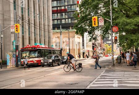 TORONTO, CANADA - 06 05 2021: Traffico su Queen Street all'incrocio di University Avenue nel centro di Toronto con un ciclista in primo piano e TTC Foto Stock