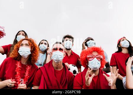 Persone multirazziali che indossano maschera protettiva guardando evento partita di calcio Foto Stock
