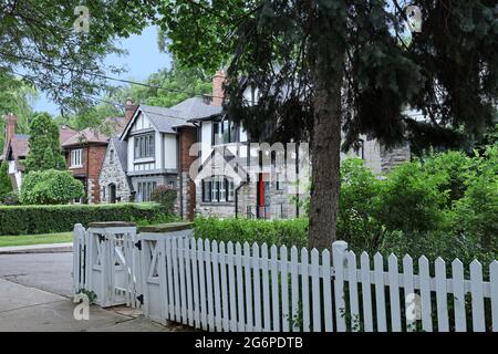 Strada residenziale alberata con vecchie case in stile Tudor a due piani e recinto bianco picket intorno al cortile anteriore Foto Stock